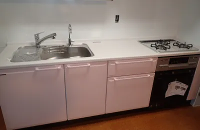 白を基調としたシステムキッチンで、シンクとガスコンロ、ビルトイン機器が横一列に配置された様子