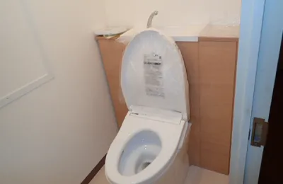 個室トイレ内に設置された白色の洋式便器で、フタが開いた状態の温水洗浄便座が写っている様子