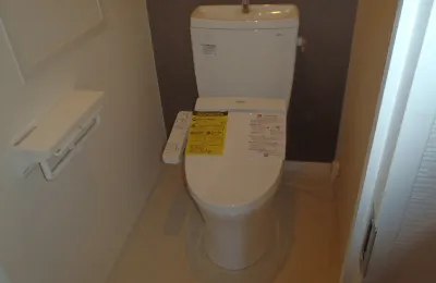 コンパクトなトイレ個室に設置された白色の温水洗浄便座付き便器で、操作リモコンとタンクが一体になった様子