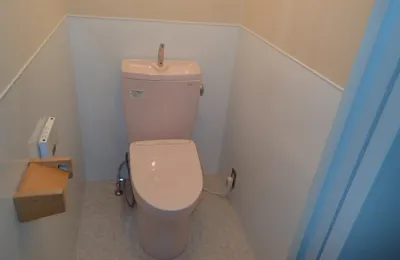 淡い色調の個室トイレ内に設置された洋式便器で、タンク付きの便器と壁付け紙巻き器が確認できる様子