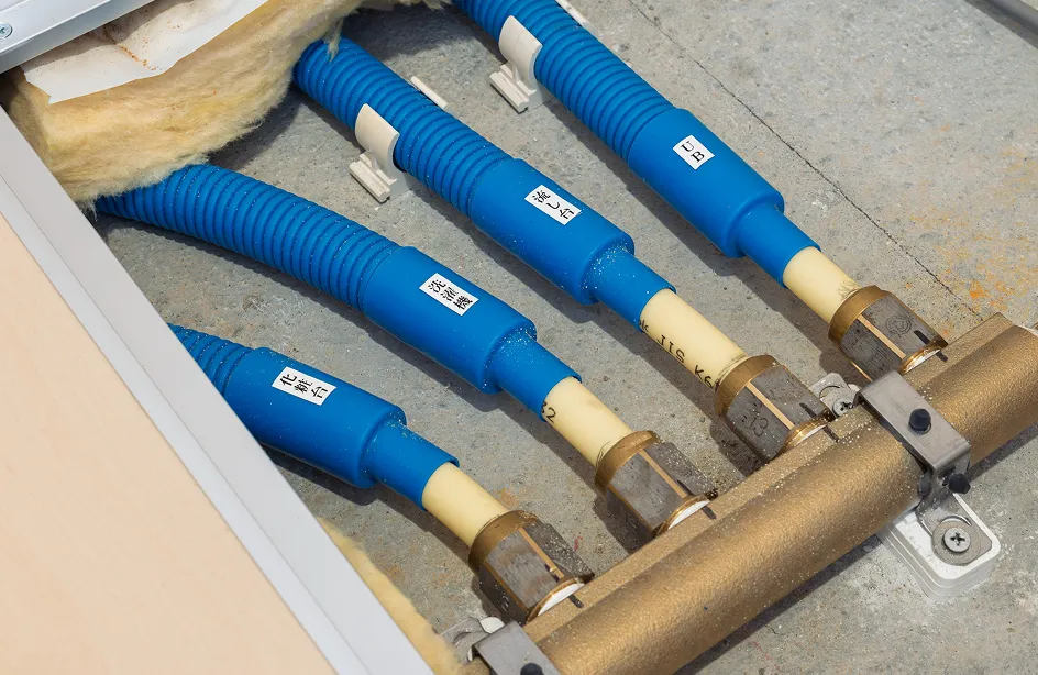 床下に設置された給水・給湯配管で、青色のフレキシブル管が分岐金具に接続され、ラベルで系統が識別されている様子