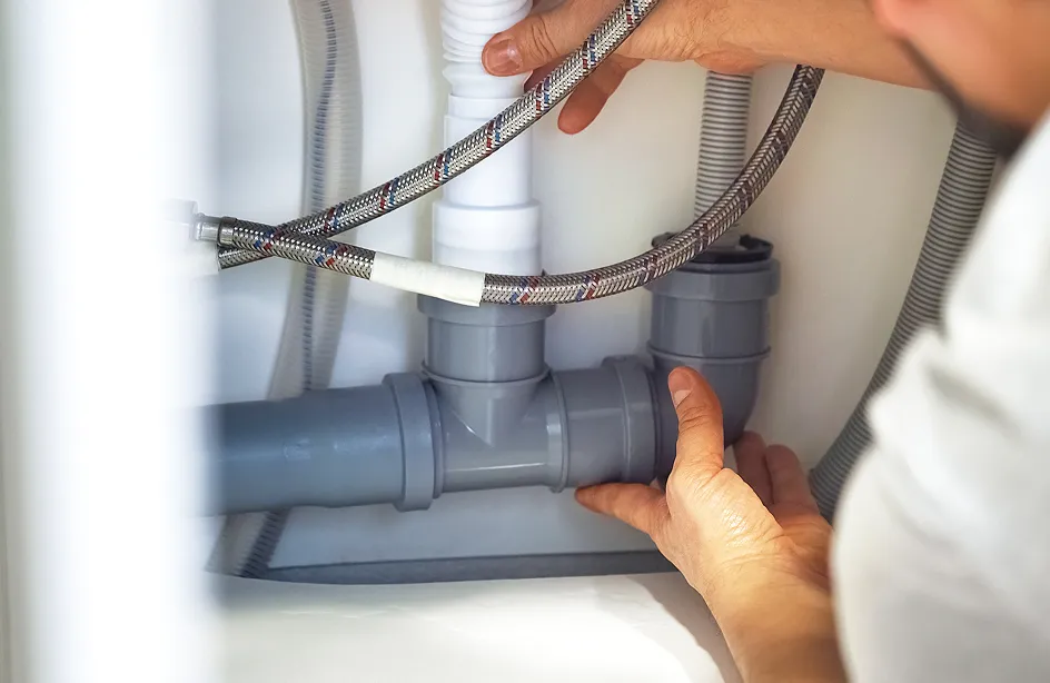 排水配管の工事現場で、作業員の手が灰色のPVC排水管を接続している様子