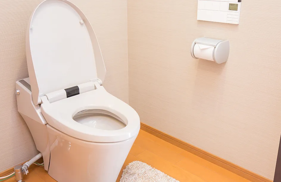 木目調の床と淡い壁紙の個室内に、フタが開いた洋式トイレとトイレットペーパーホルダーが配置された様子