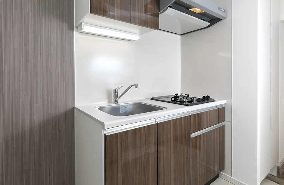 コンパクトな室内キッチンで、シンクとガスコンロ、換気扇が一体化したシステムキッチンが設置されている様子