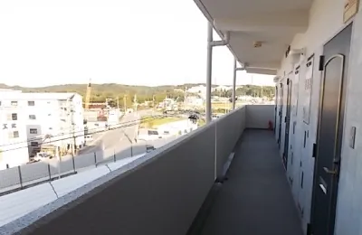 集合住宅の外廊下を写した写真で、各住戸の玄関ドアが並び、手すり越しに周囲の街並みが見える共用部の様子