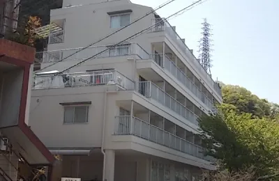 住宅街に建つマンションの外観を写した画像で、手すり付きバルコニーとシンプルな箱型の建築デザインが特徴