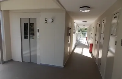 集合住宅の共用廊下内部を写した写真で、左側にエレベーター扉、右側に各住戸の玄関が並ぶ様子