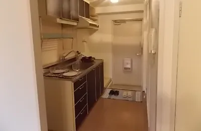 玄関から続く細長いキッチンスペースで、シンクとコンロ、吊戸棚が一直線に配置されたコンパクトな台所