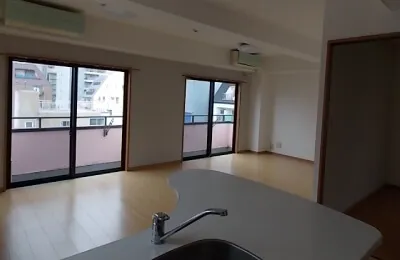 キッチンカウンター越しに広がるリビングダイニングで、大きな窓からバルコニーと外の景色が見える明るい室内