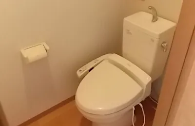 狭いトイレ個室に設置された白色の温水洗浄便座付き便器で、タンクと一体型のシンプルな設備構成